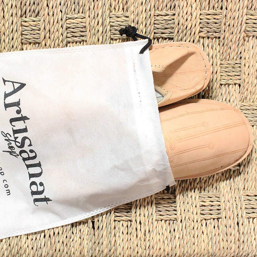 Natural leather babouches and an Artisanat Shop bag arranged on woven straw