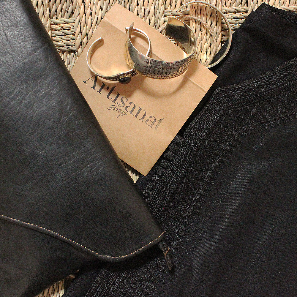 Black Moroccan leather accessories arranged with an Artisanat Shop card on woven straw