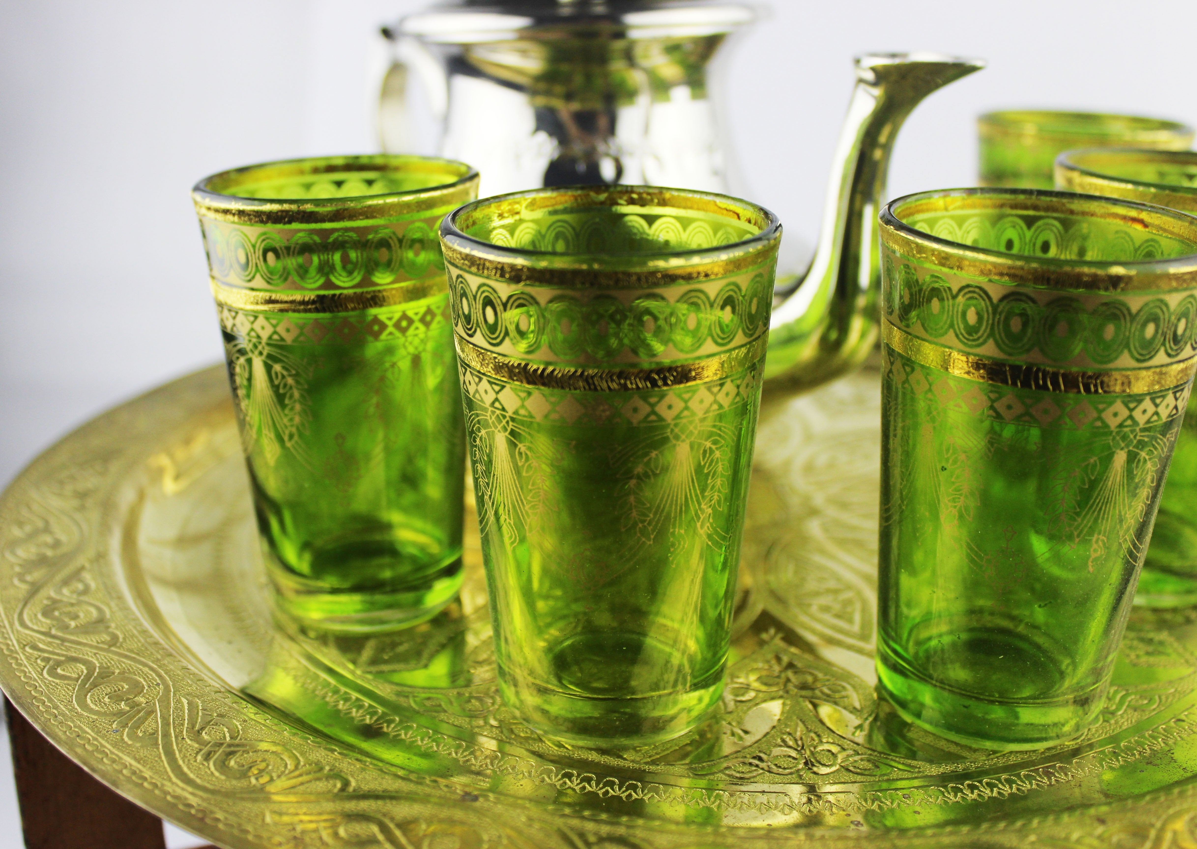 Green Moroccan tea glasses arranged with a silver teapot on an engraved tray